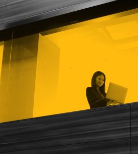 Woman working on laptop, seen through office window