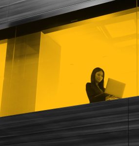 Woman working on laptop, seen through office window